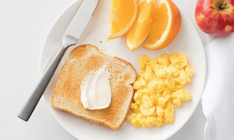 plate with buttered bread, eggs, orange slices and an apple on the side